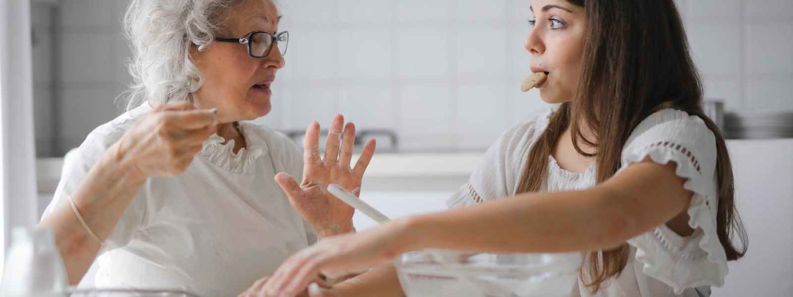 pensive grandmother with granddaughter having interesting conversation while cooking together in light modern kitchen
