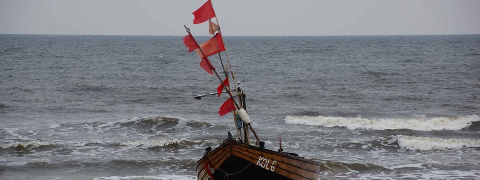 brown boat with red flags on the seashore