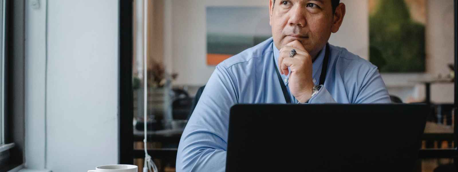 thoughtful ethnic businessman using laptop while working in office