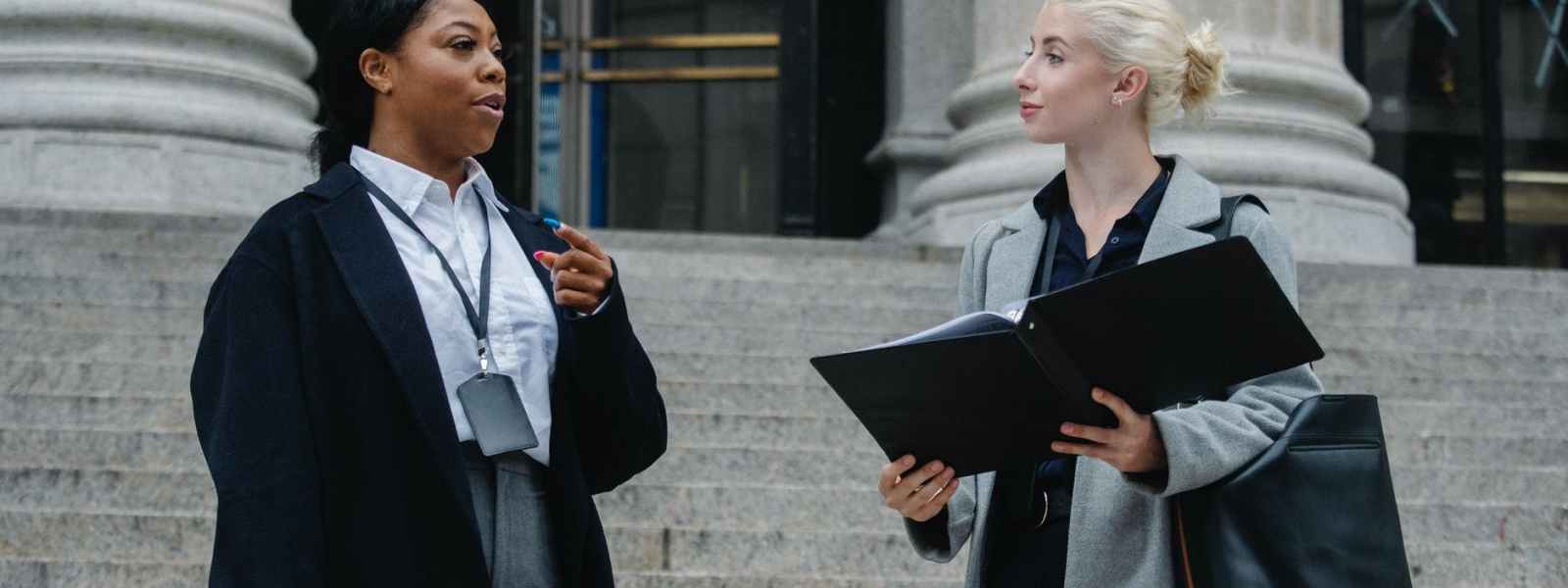 elegant diverse female business partners with documents talking on street