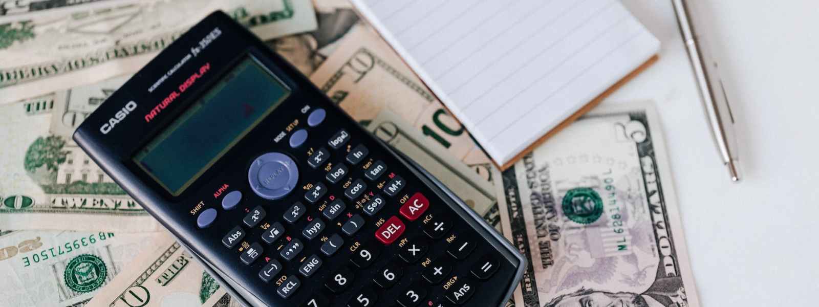 calculator and notepad placed on usa dollars stack