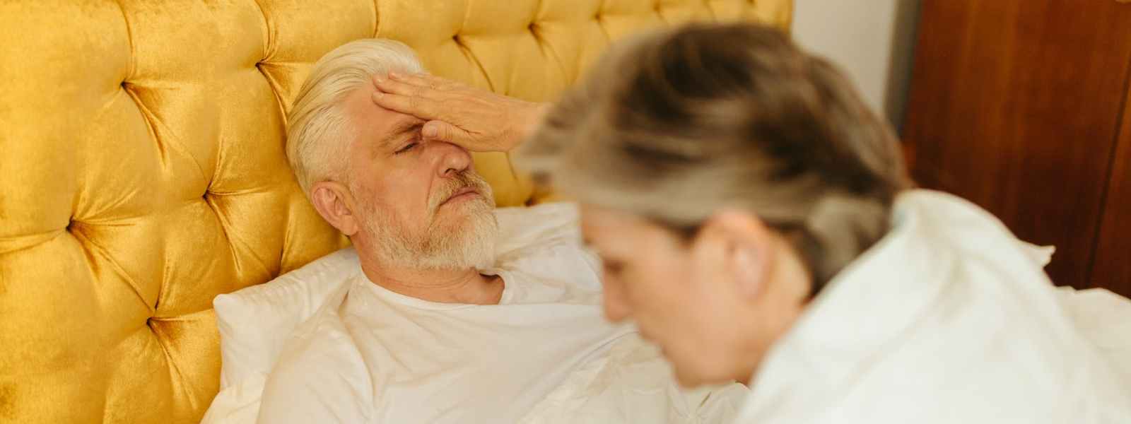 elderly man lying down on bed looking sick