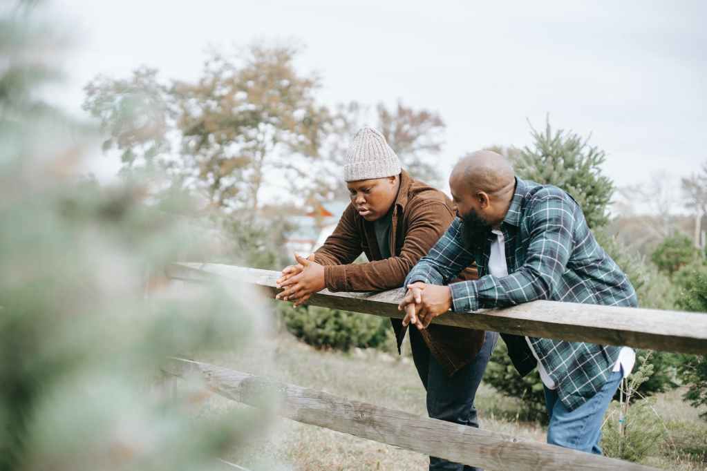 black father conversing with teenager near fence on farmland