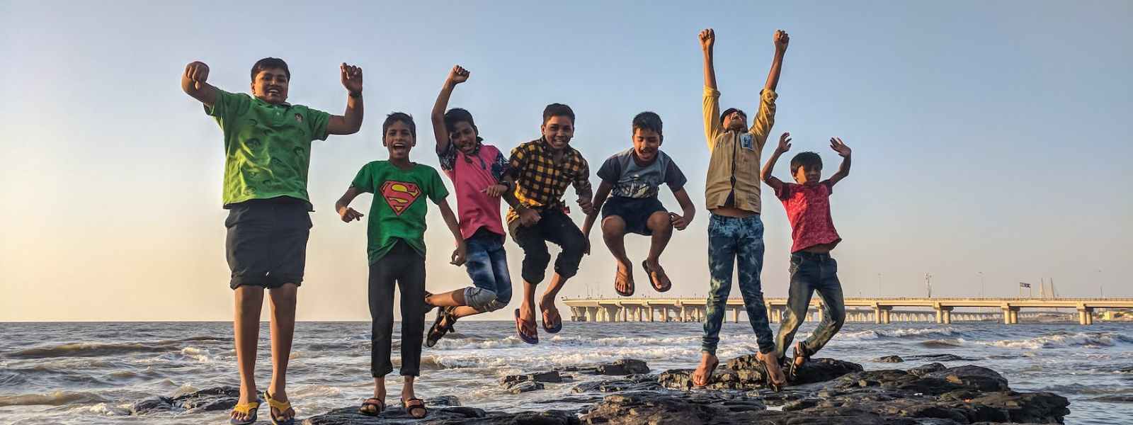 boy wearing green crew neck shirt jumping from black stone on seashore