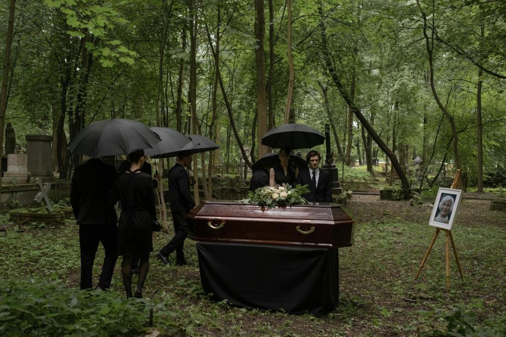 brown coffin surrounded by people in black clothes