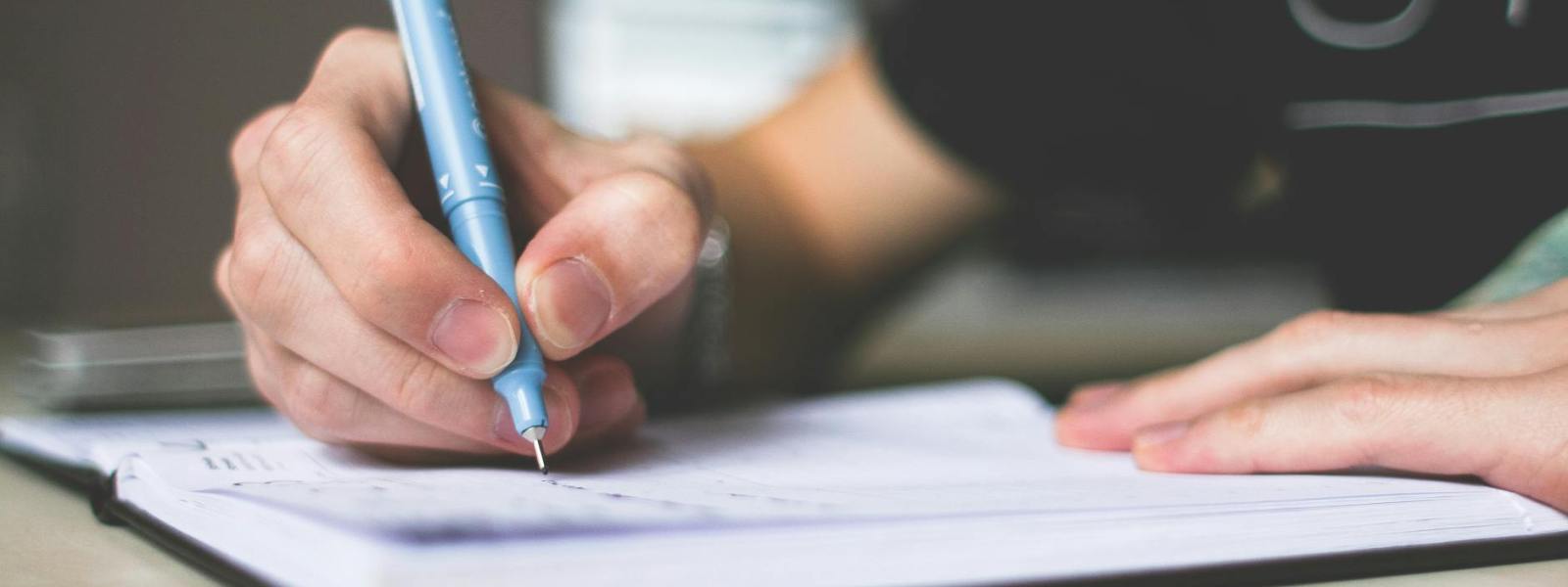 person holding blue ballpoint pen writing in notebook