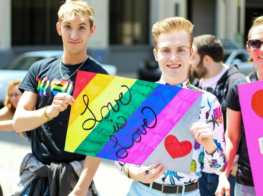three men holding assorted painted love is love banner